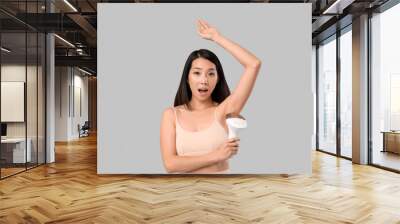 Surprised Asian woman with photoepilator on grey background Wall mural