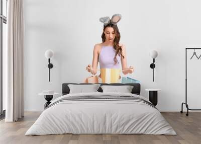 Surprised young woman in Easter bunny ears headband with shopping bags on white background Wall mural