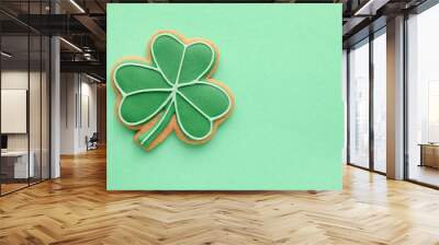 Tasty gingerbread cookie in shape of clover leaf for St. Patrick's Day celebration on green background Wall mural