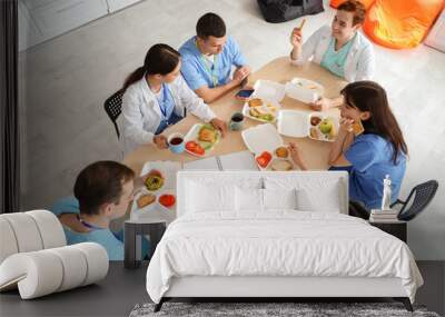 Team of doctors having lunch at table in hospital kitchen, top view Wall mural