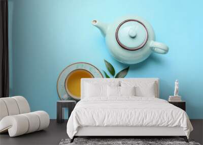 Teapot and cup of tea with green leaves on color background Wall mural