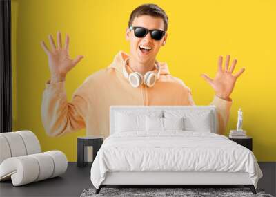 Teenage boy in sunglasses with headphones on yellow background Wall mural