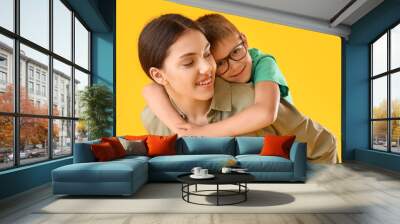 teenage girl carrying backapack her little brother on yellow background Wall mural