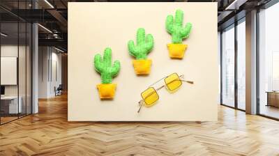 Toy cacti with stylish sunglasses on light background Wall mural