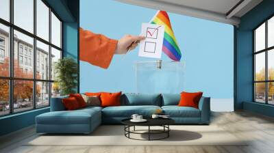 Voting woman with LGBT flag near ballot box on table against blue background Wall mural