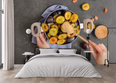 Woman adding sugar into pot with plums on dark background Wall mural