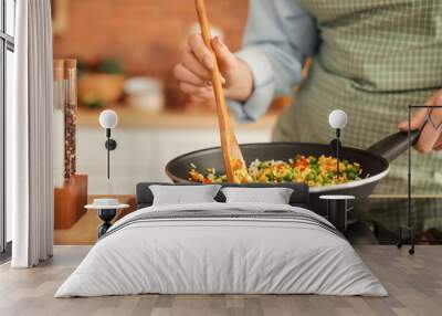 Woman cooking tasty rice with vegetables on stove in kitchen, closeup Wall mural