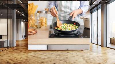 Woman cooking tasty rice with vegetables on stove in kitchen, closeup Wall mural