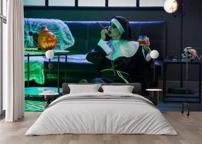 Woman dressed for Halloween as nun with alcohol and cigar in decorated room Wall mural