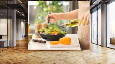 Woman dressing fresh vegetable salad with olive oil in kitchen Wall mural