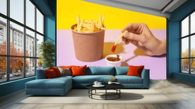 Woman eating tasty french fries with sauce on color background Wall mural