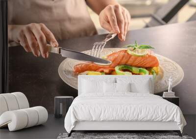 Woman eating tasty salmon with fresh peppers at table Wall mural