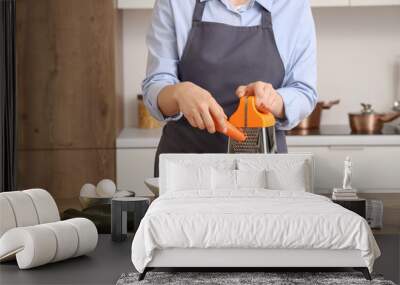 Woman grating carrot at table in kitchen, closeup Wall mural