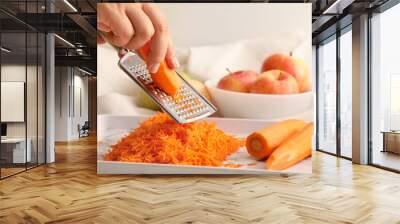 Woman grating carrot on light background Wall mural