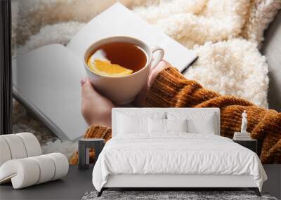 Woman holding cup of tea and opened book on fluffy plaid Wall mural