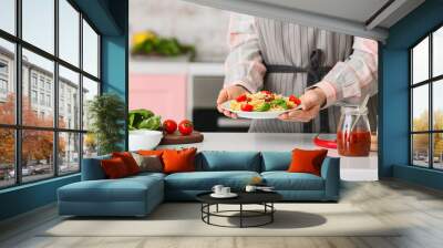 Woman holding plate with tasty pasta in kitchen, closeup Wall mural