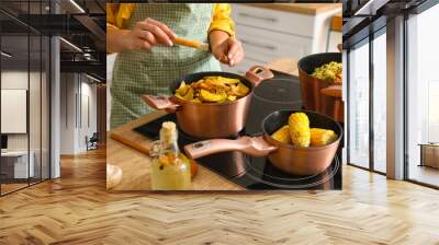 Woman in apron adding spices to cooking pot with vegetable stew in kitchen, closeup Wall mural