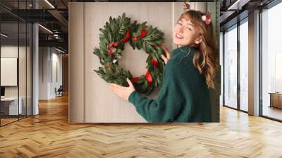 Woman in green sweater hanging Christmas mistletoe wreath on door Wall mural