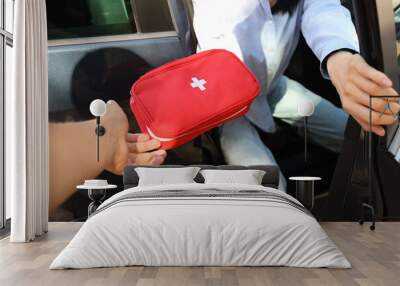 Woman on passenger seat passing first aid kit to person outside car Wall mural