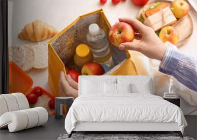 Woman packing meal into lunch box bag on light background, closeup Wall mural