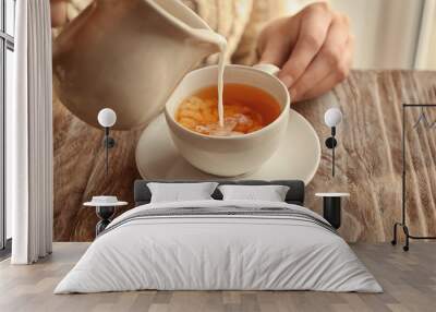 Woman pouring milk into cup with aromatic tea on table Wall mural