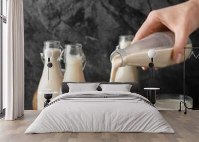 woman pouring tasty vegan milk from bottle into glass on grey background Wall mural