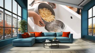 Woman pouring water from boiled pasta into colander in sink Wall mural