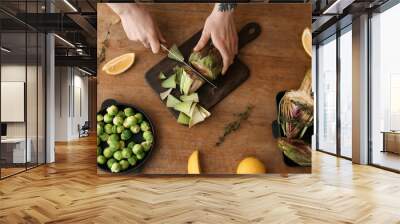 Woman preparing tasty raw artichokes on wooden table Wall mural