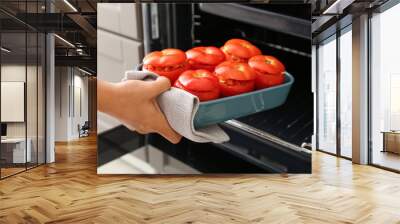 Woman putting baking dish with uncooked stuffed tomatoes in oven, closeup Wall mural