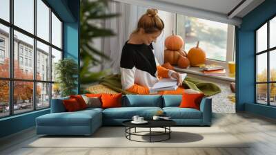 Woman reading book at home on autumn day Wall mural