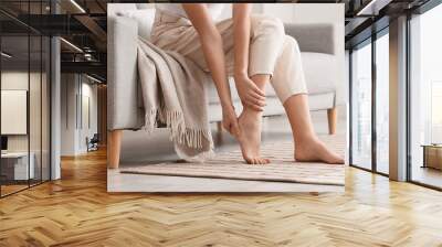 Woman sitting on sofa and making foot massage in room, closeup Wall mural