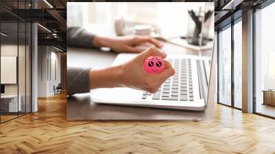 Woman squeezing stress ball with drawn cute face in office Wall mural