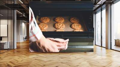 Woman taking baking tray with cookies out of oven Wall mural