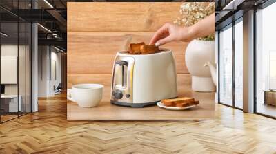 Woman taking bread slice from white toaster near wooden wall Wall mural