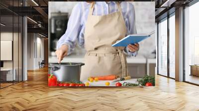 Woman with cook book preparing food in kitchen Wall mural