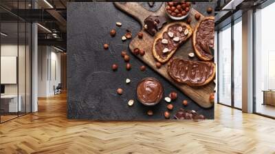 Wooden board of bread with chocolate paste and hazelnuts on black background Wall mural