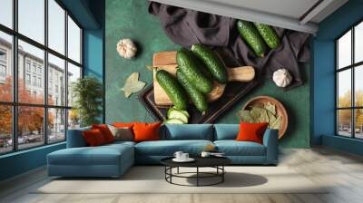 Wooden board with fresh cucumbers, garlic and bay leaves on green background Wall mural