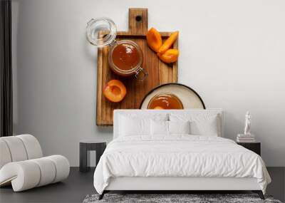 Wooden board with glass bowl and jar of sweet apricot jam on white background Wall mural