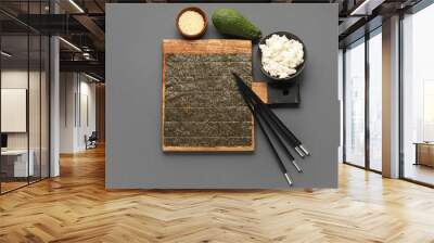 Wooden board with nori sheet, bowl of rice, sesame seeds, avocado and chopsticks on dark background Wall mural