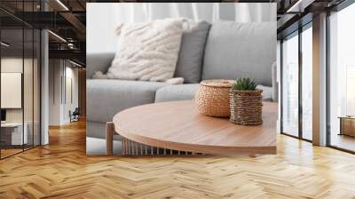 Wooden coffee table with with houseplant and wicker basket near grey sofa in living room Wall mural