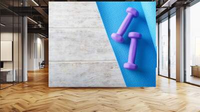 Yoga mat with dumbbells on light wooden background Wall mural