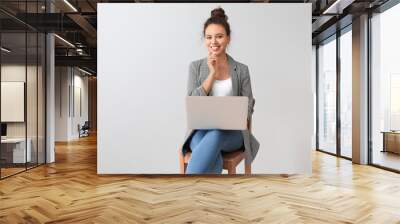 Young African-American businesswoman with laptop sitting on chair near grey wall Wall mural