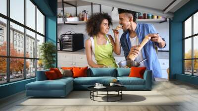 Young African-American couple tasting food while cooking together in kitchen Wall mural