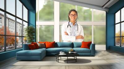 Young African-American female doctor in eyeglasses with stethoscope near window in clinic Wall mural