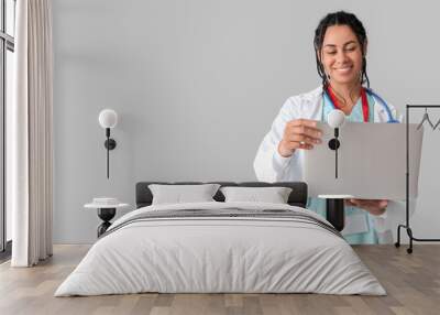 Young African-American female doctor with stethoscope and laptop on white background Wall mural