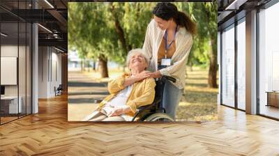 Young African-American female medical worker with elderly woman on wheelchair outdoors Wall mural