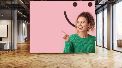 Young African-American woman pointing at something and drawn smile on pink background Wall mural