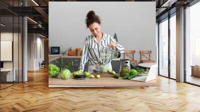 Young African-American woman pouring fresh smoothie into cup in kitchen Wall mural