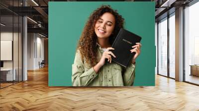 Young African-American woman with Holy Bible on green background Wall mural