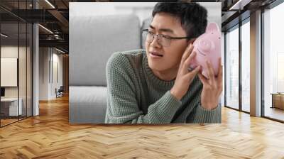 Young Asian man with piggy bank at home, closeup Wall mural